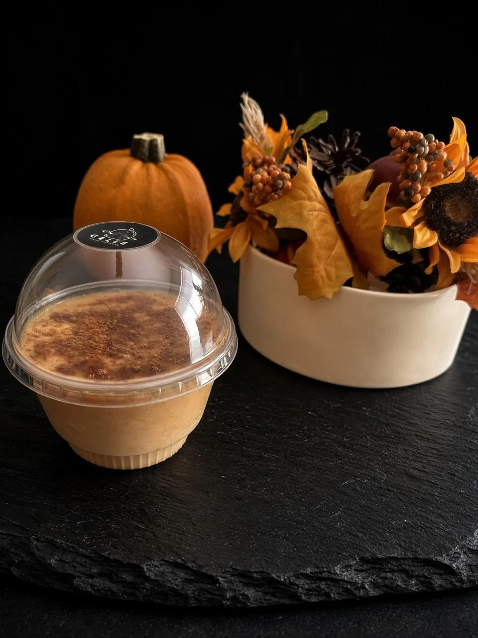 Gelée alta en proteína sabor pumpkin spice, en vaso individual con tapa de domo y canela espolvoreada, junto a una calabaza y hojas de otoño